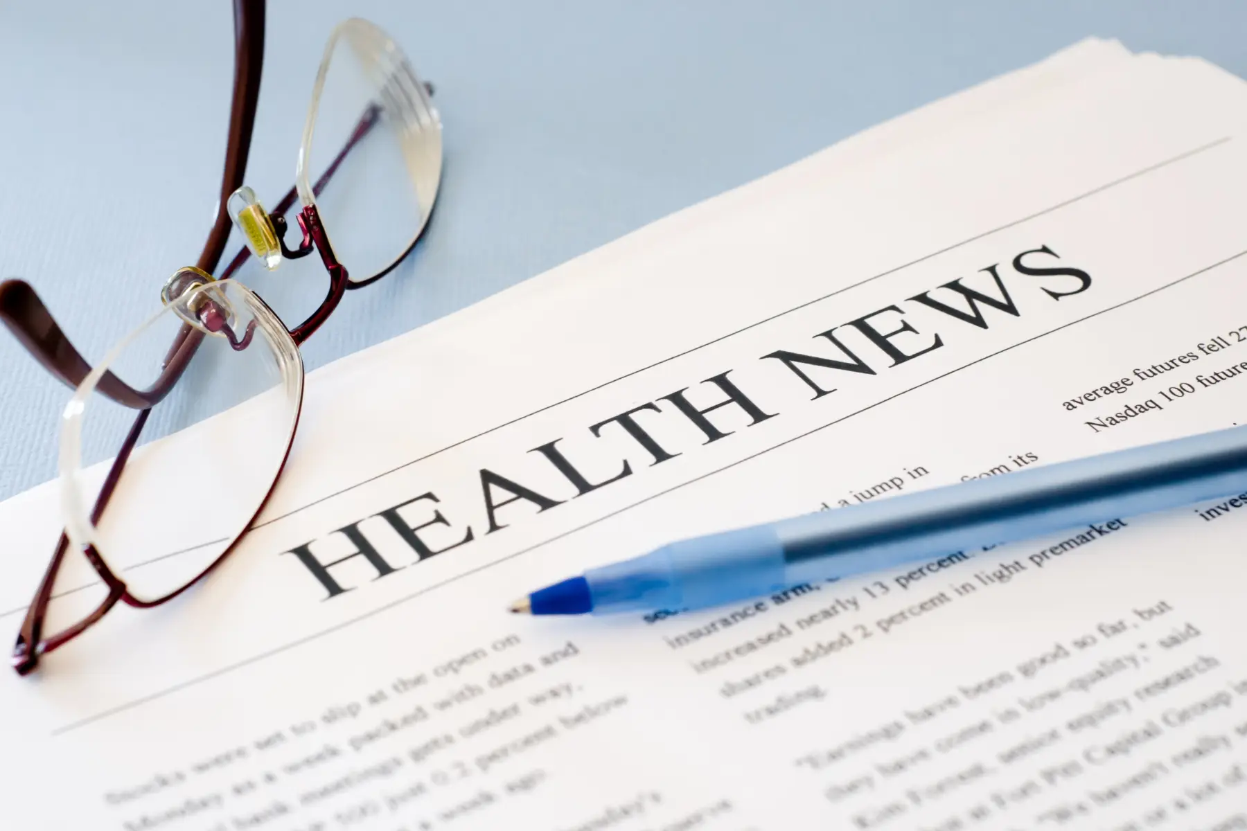 Health news, glasses, and pen on blue background.